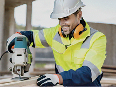 Um trabalhador da construção civil usando um capacete e colete de segurança operando uma furadeira pesada em um canteiro de obras.